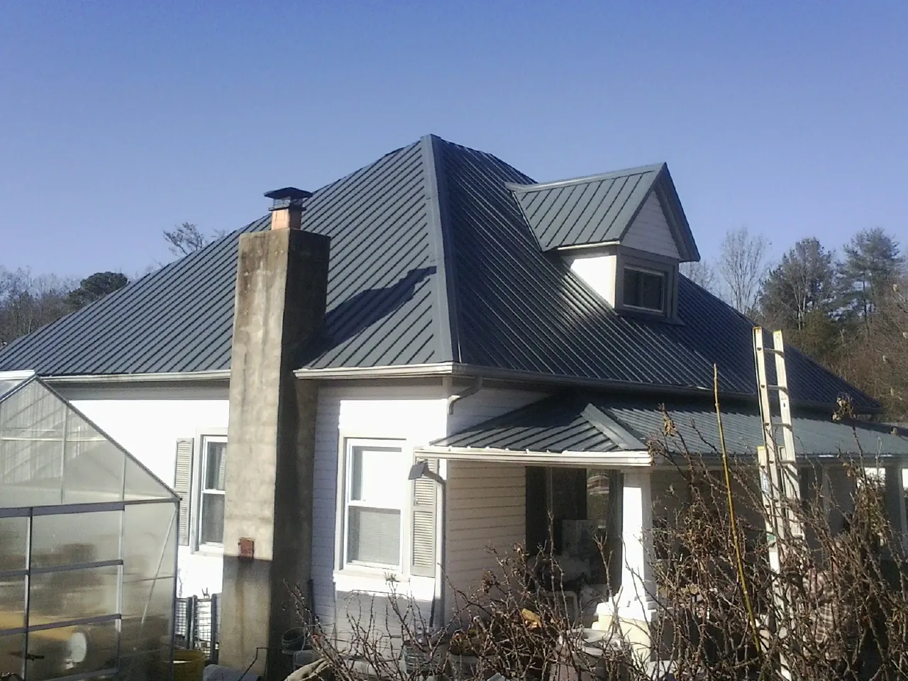 Dark blue standing seam metal roof on a white farmhouse with dormer — Slate & Tile Roof Repair by Roofing Brothers in West Hollywood