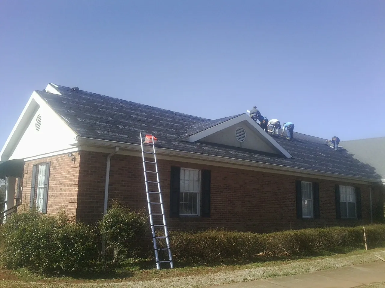 Crew tearing shingles off a brick ranch roof with a ladder set — Emergency Roof Repair work by our crew in West Hollywood