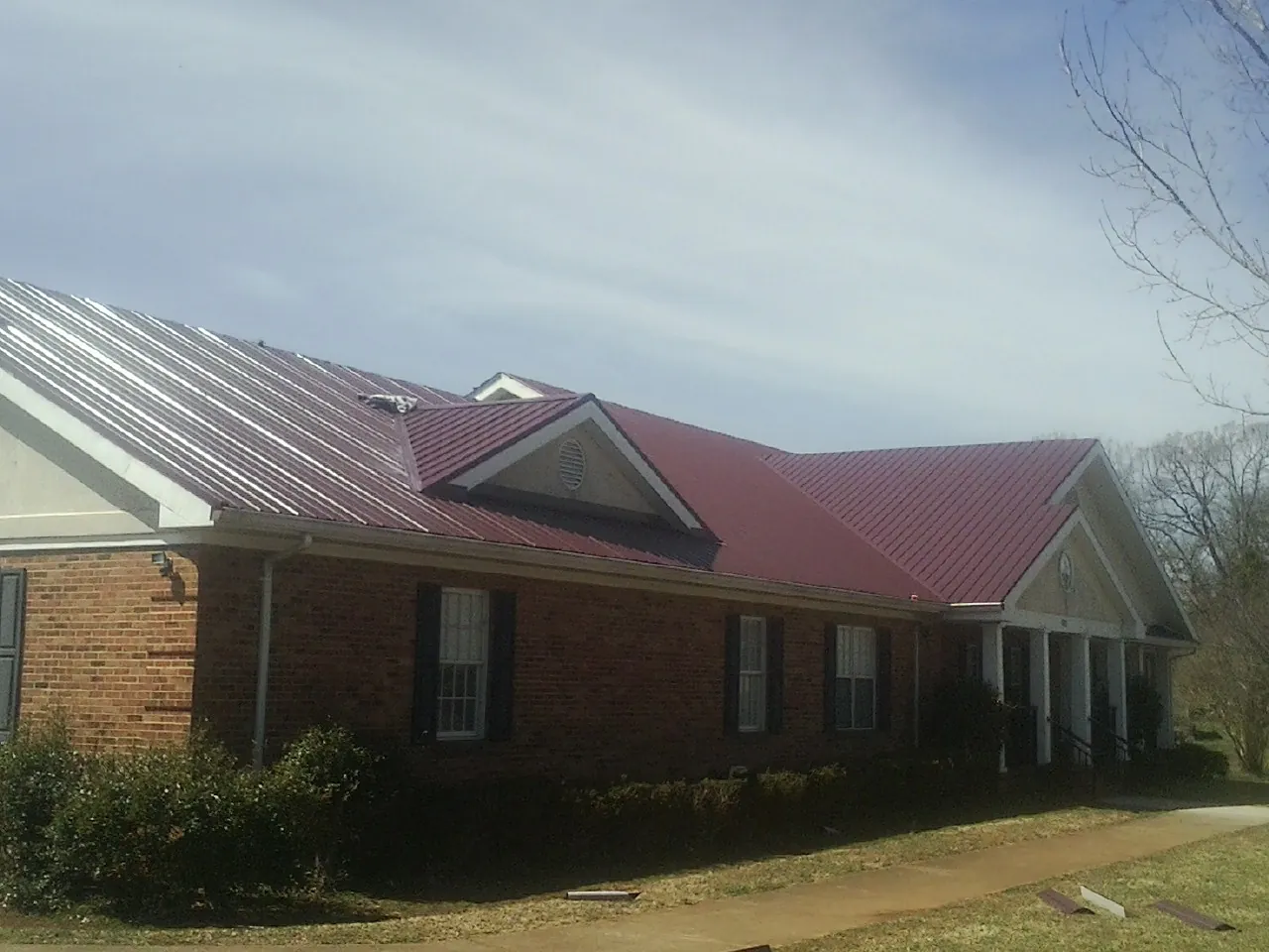Red metal roof with gabled entries on a long brick building, from a Hail Damage Roof Repair job in West Hollywood