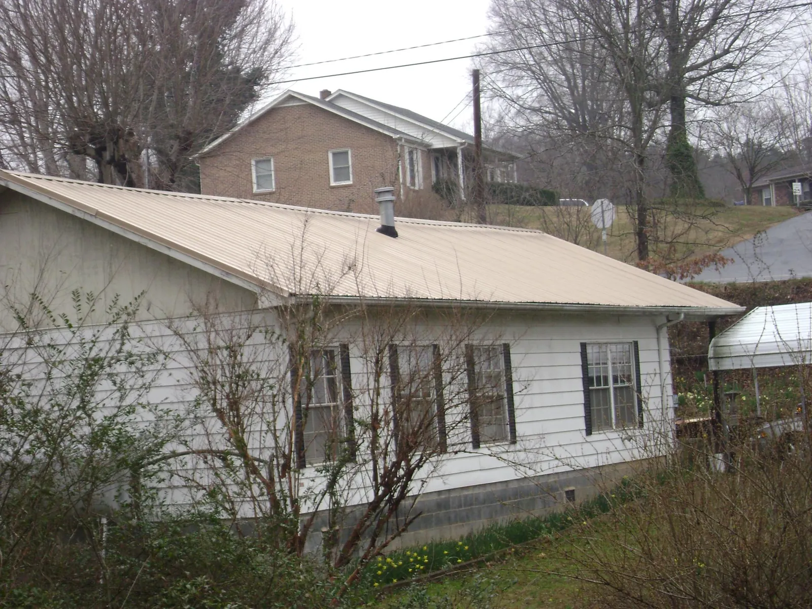 Tan metal roof on a white sided house set into a hillside — Commercial Roofing by Roofing Brothers in West Hollywood